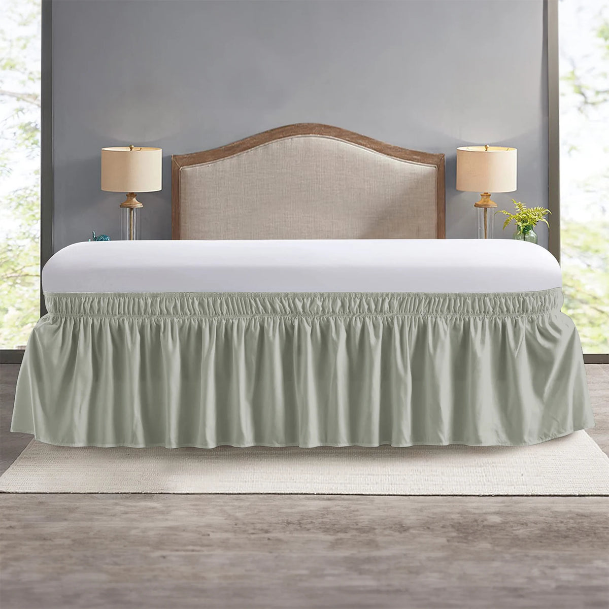 A light sage green elastic wrap-around bed skirt with ruffles displayed over a white bed frame.