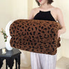 A woman holds a dark brown leopard print plush jacquard throw blanket against her chest.
