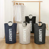 Three large fabric laundry bags in navy, white, and black hanging on a wooden rack.