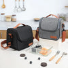 A gray insulated lunch bag with brown straps rests on a white table next to various kitchen utensils and food items.