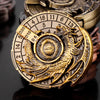 A close-up of a brass metal spinner dice cube with numbered faces and an embossed dragon design.