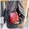 A woman holds a vintage brown PU leather crossbody handbag against a gray blazer.