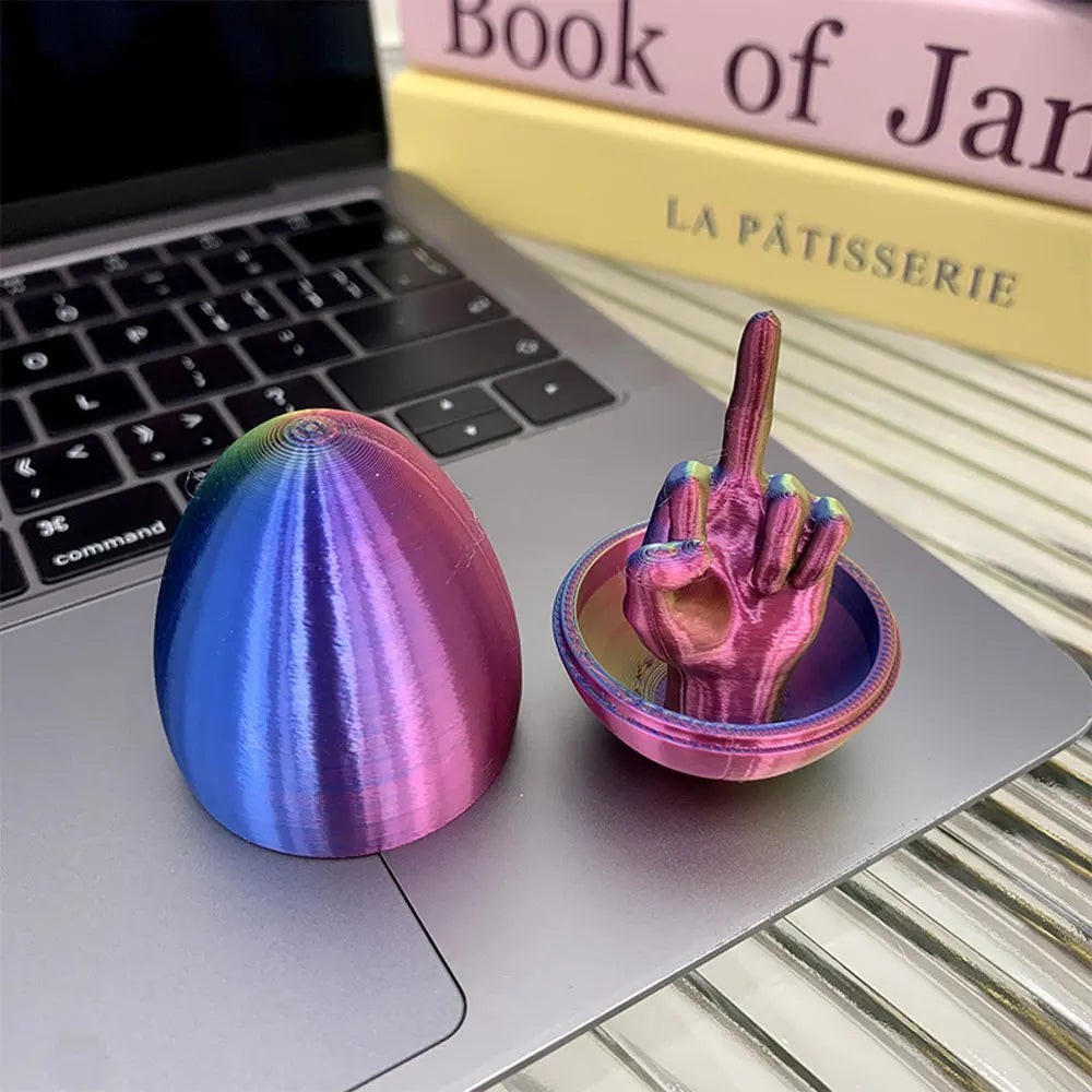 A pink and blue egg shaped desk decor featuring a hand gesture on a silver laptop.