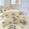 A set of two floral cotton pillowcases in pale yellow with purple and green floral patterns on a bed.