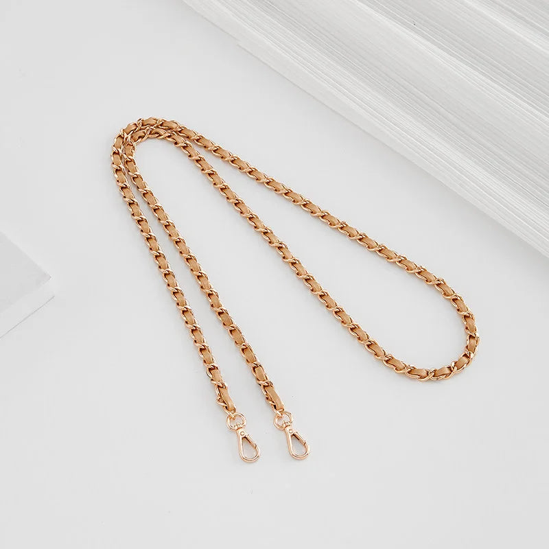 A close-up of a gold-toned metal chain strap with adjustable buckles, laid diagonally on a white surface.