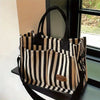 A striped canvas tote bag with inner pockets hanging in a window frame.
