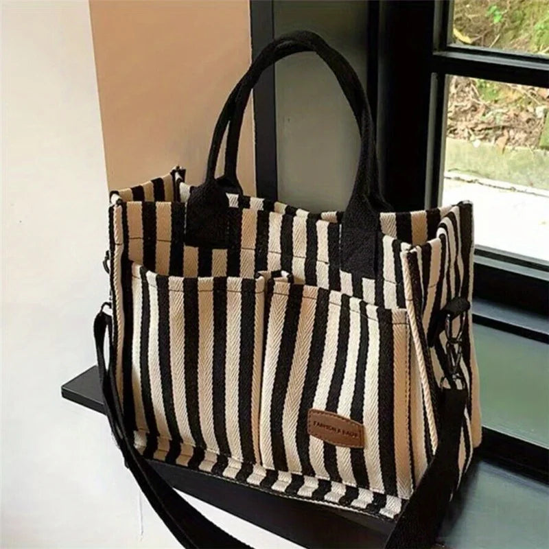 A striped canvas tote bag with inner pockets hanging in a window frame.
