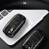 Close-up view of a black carbon fiber car key cover resting on a white laptop keyboard.