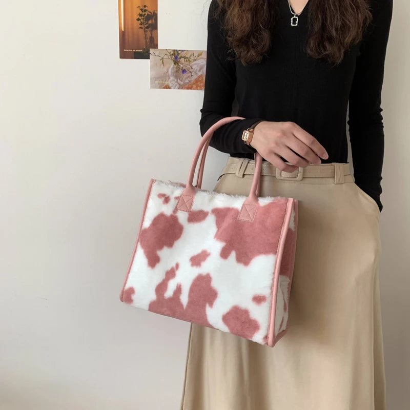 A woman holds a pink and white faux fur leopard print tote bag against a light background.