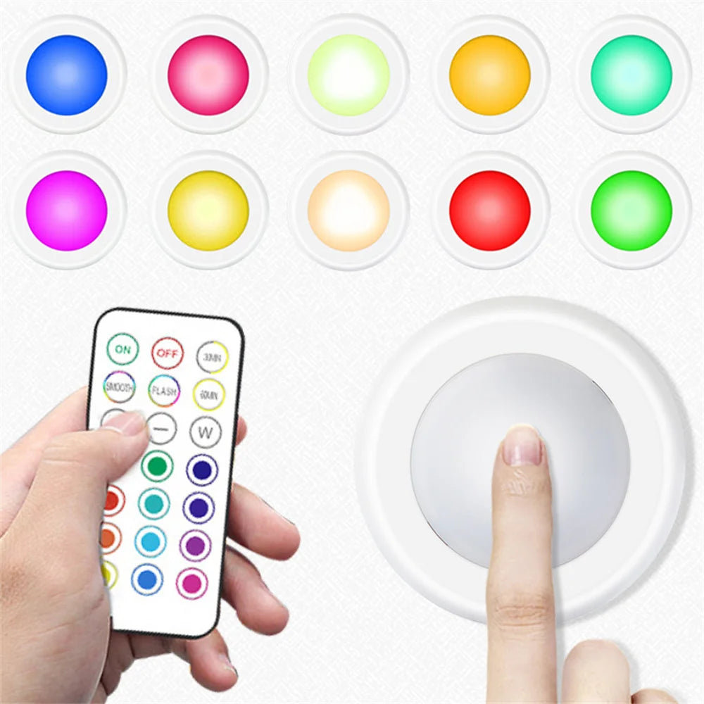 A hand holds a smartphone displaying various color options, next to a white light switch and several colored LED lights.
