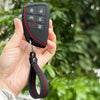 A hand holds a black silicone key fob cover with various buttons attached to a keyring.