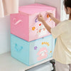 A person is holding a pink and blue foldable storage box with happy designs, next to a white cabinet.