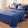A blue striped satin bed sheet set with matching pillows is displayed on a wooden bed frame.