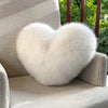 A fluffy white heart-shaped throw pillow resting on a light gray upholstered chair.
