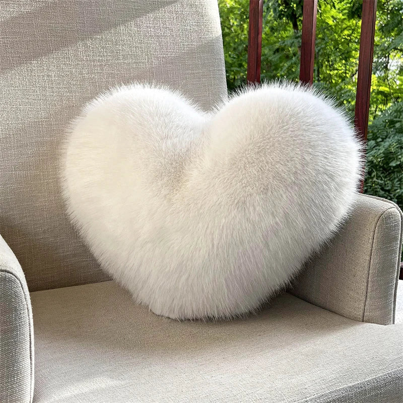 A fluffy white heart-shaped throw pillow resting on a light gray upholstered chair.