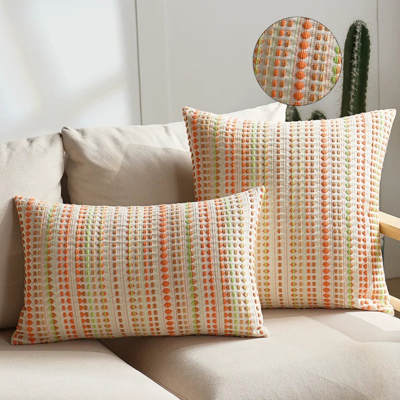 Two square linen pillow covers in a multicolored geometric pattern featuring orange, green, and white tones.