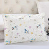 A white cartoon patterned pillowcase with various animal and nature motifs resting on a white surface.