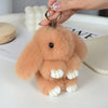 A fluffy, light brown bunny keychain with a pom pom tail is being held by a hand.