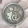 Silbermünze mit stilisiertem chinesischem Koi-Symbol und geometrischem Rand in der Hand.