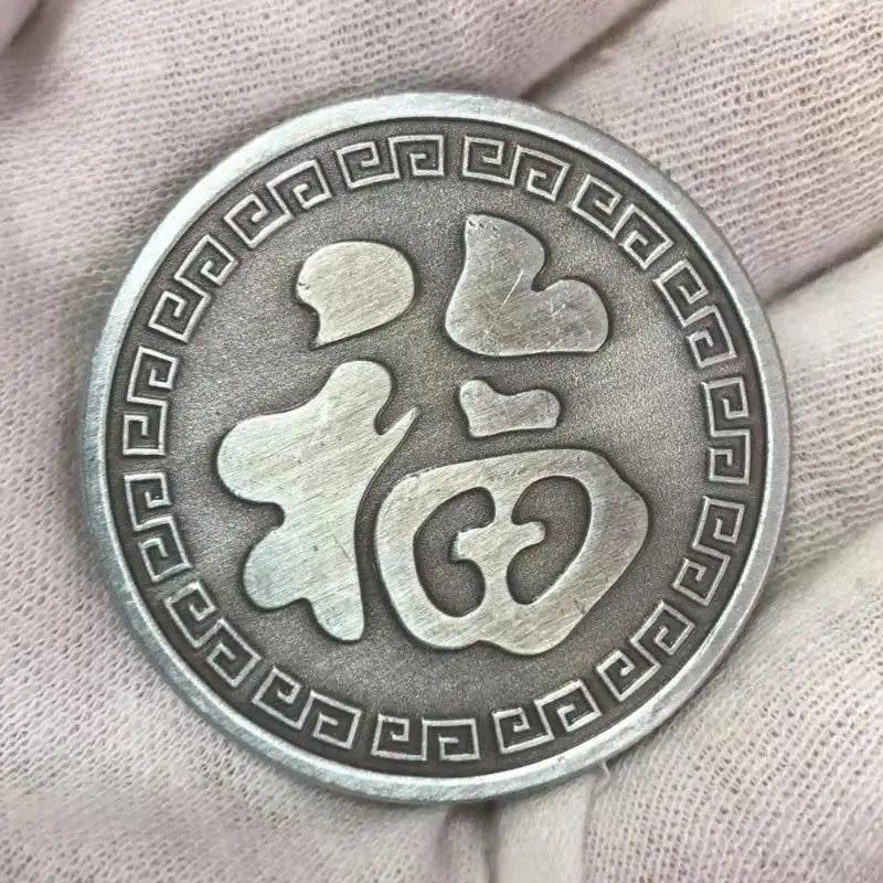 Silbermünze mit stilisiertem chinesischem Koi-Symbol und geometrischem Rand in der Hand.