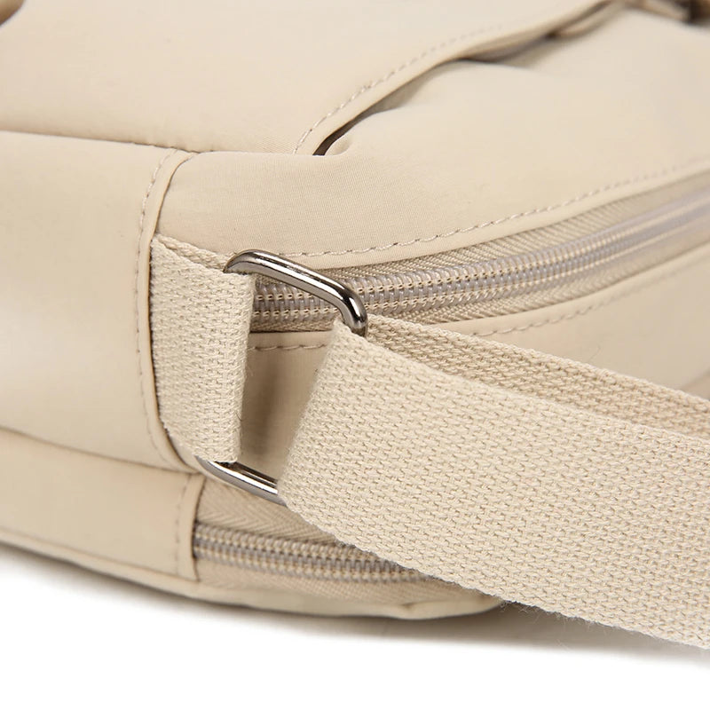 A close-up view of a beige nylon crossbody bag with a silver zipper and strap detail.