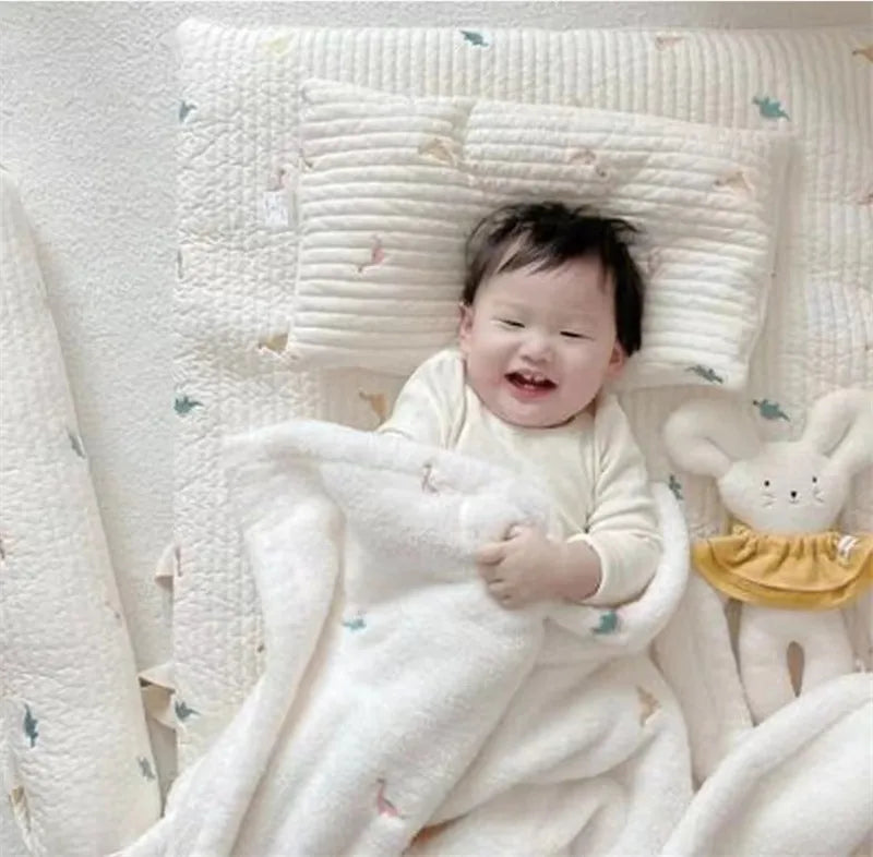 A baby is wrapped in a white coral fleece blanket with bear embroidery.