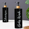 A black refillable shampoo and lotion dispenser bottle with a wooden cap and white script text on the side.