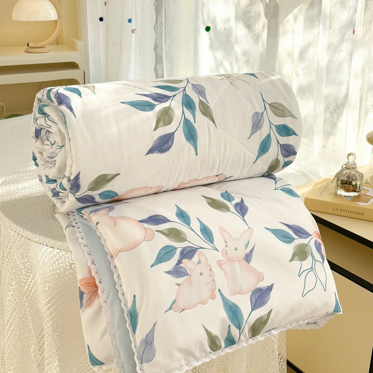 White comforter with a panda print featuring pink rabbits and green leaves, displayed near a window.