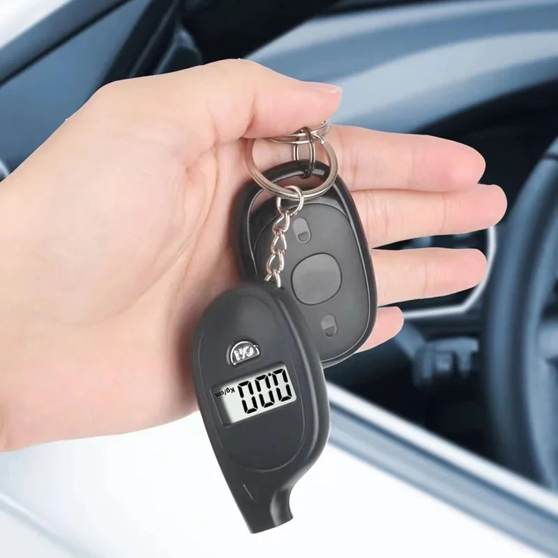 A hand holds a black digital tire pressure gauge with an LCD display and metal keyring.