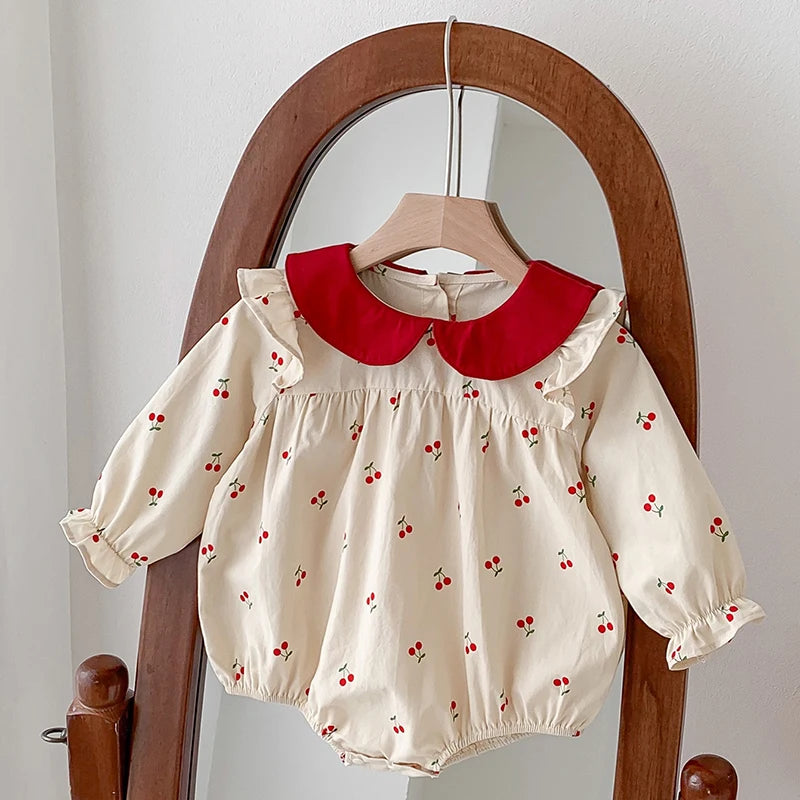 A cream-colored baby girl floral lace cotton romper with a red Peter Pan collar displayed on a wooden hanger.