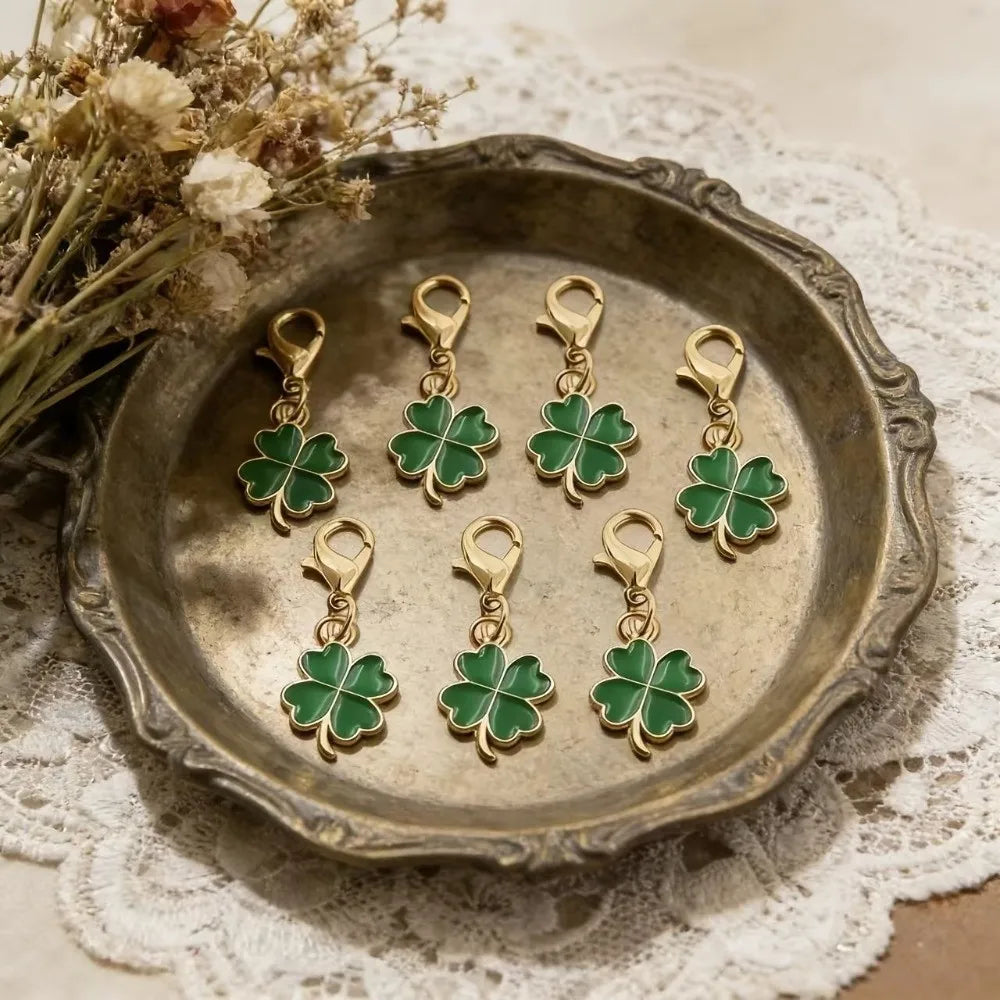 Gold-toned four-leaf clover keychain charms displayed on a rustic metal plate with dried flowers.