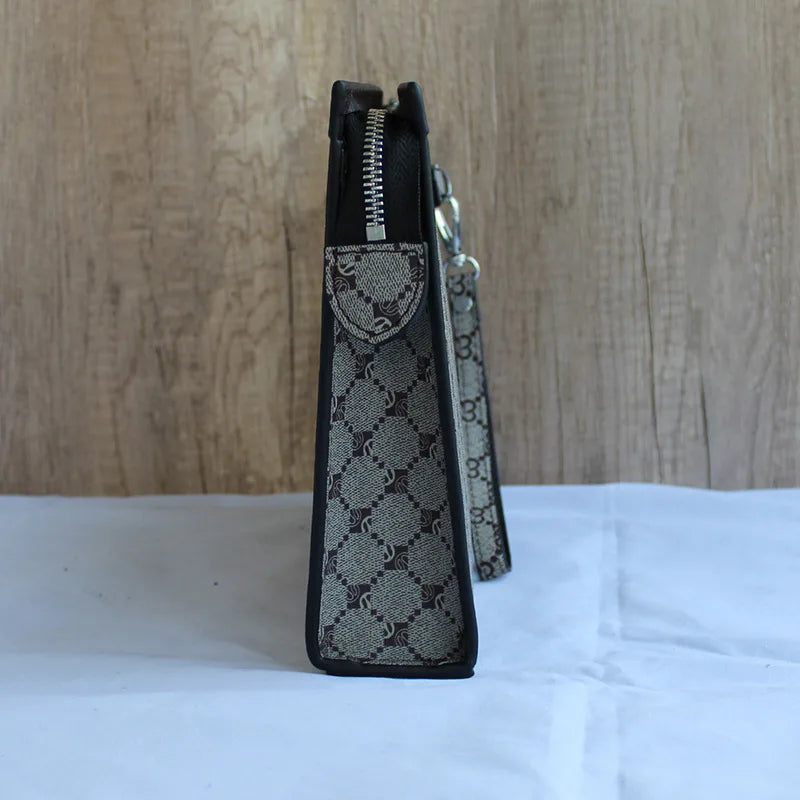 A black designer clutch bag with a zippered top and a patterned fabric detail resting on a white surface.