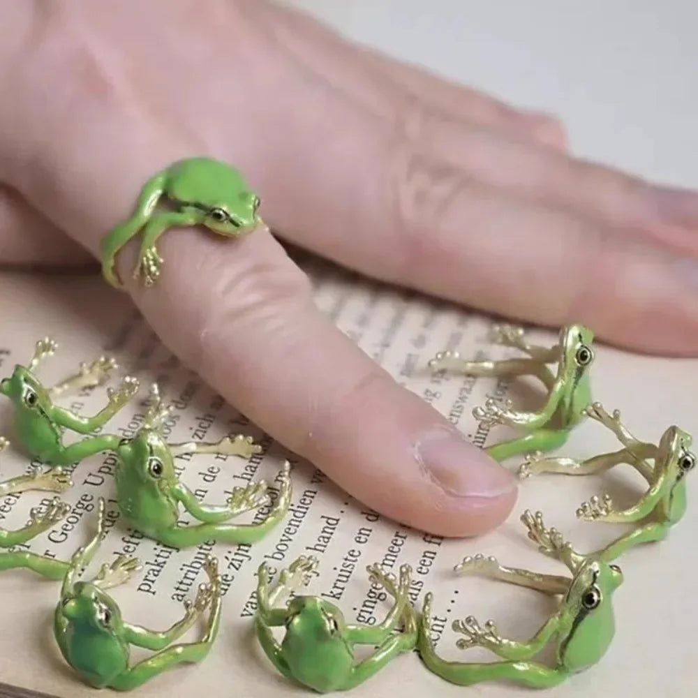 A hand wearing a cute green tree frog ring on the finger, displayed against a light background.