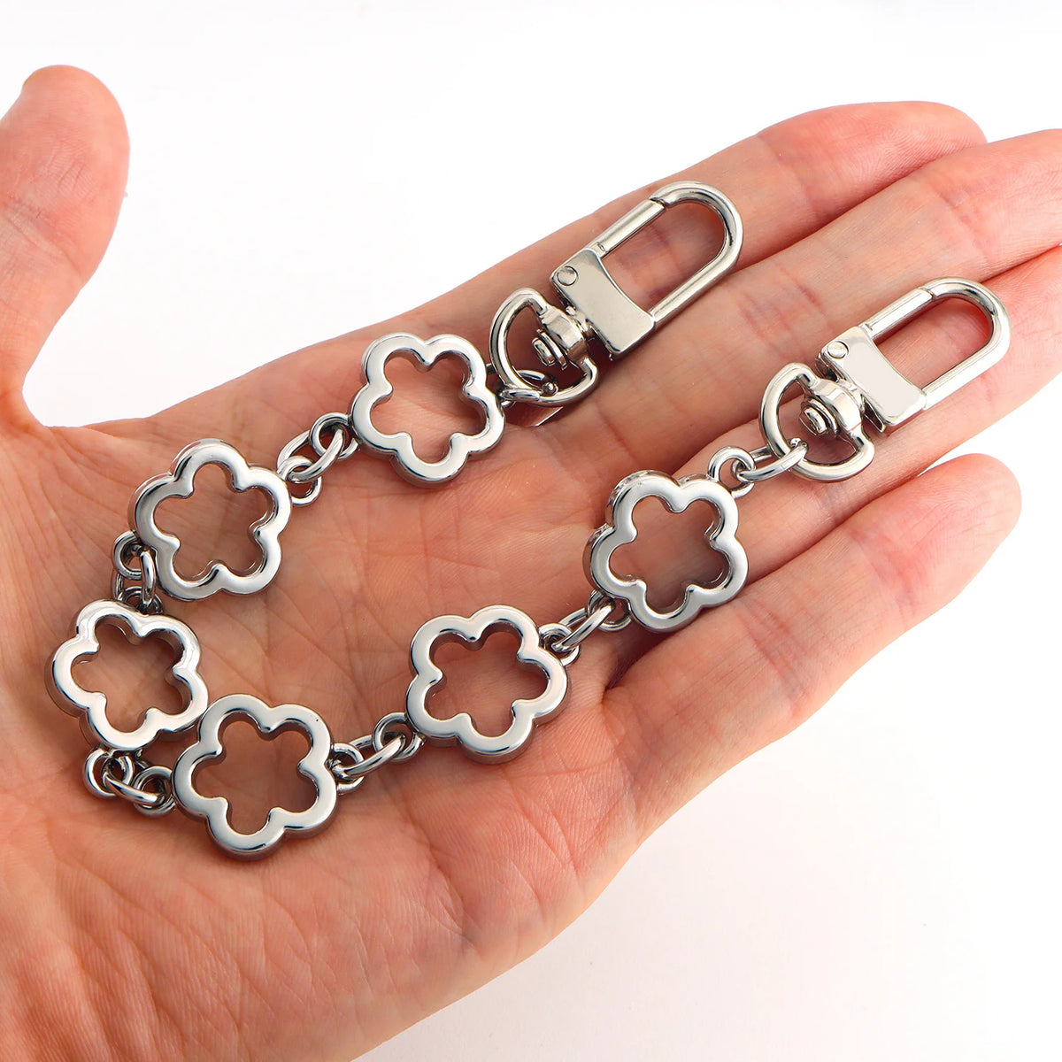 Silver adjustable flower bag chain extender for handbags and DIY purses held in a hand.