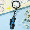 A black keychain shaped like a blue Ford Bronco, resting on a light yellow background with pink cloud shapes.