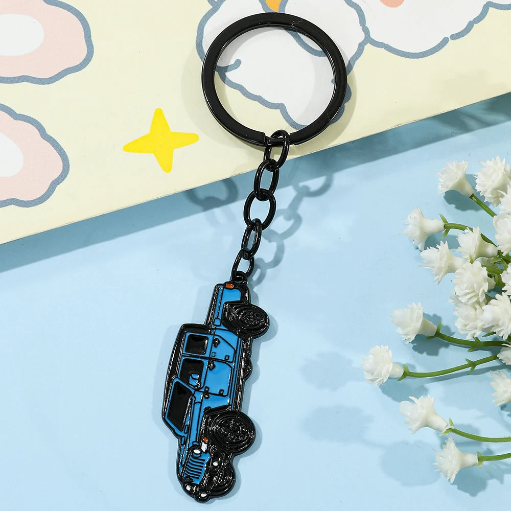 A black keychain shaped like a blue Ford Bronco, resting on a light yellow background with pink cloud shapes.