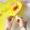 Hands are opening a yellow cartoon duck bath toy storage mesh bag to reveal a white suction cup.