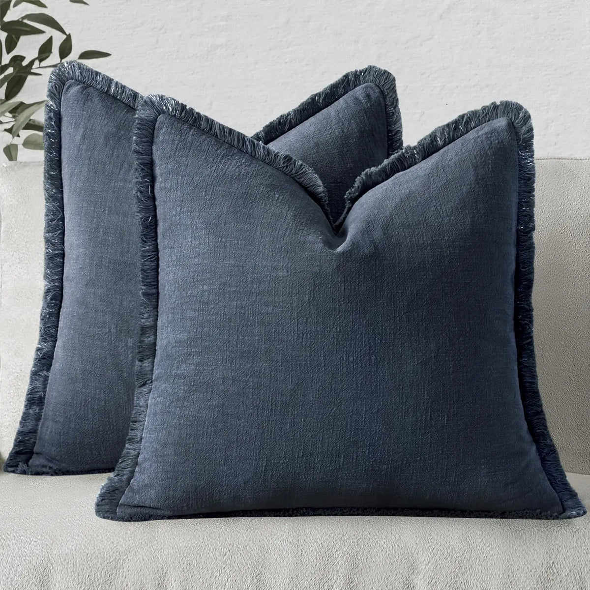 A dark blue linen throw pillow cover with fringe detail resting on a light gray sofa.
