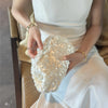 A person holds a white sequin beaded chain shoulder clutch bag in front of their torso.