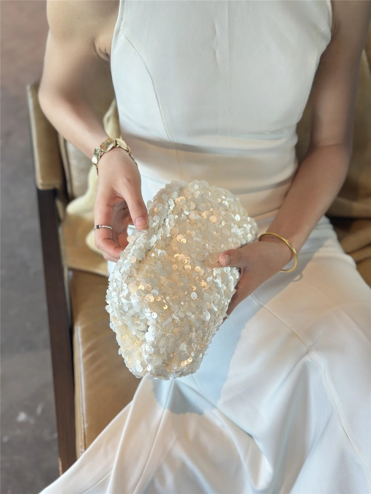 A person holds a white sequin beaded chain shoulder clutch bag in front of their torso.