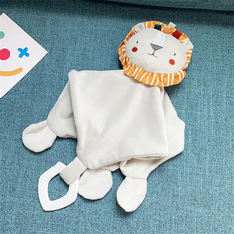 A white elephant plush toy with an orange and striped hood, teether, rattle, and comfort blanket lying on a blue fabric.