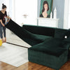 A dark emerald green plush velvet elastic sofa cover is shown draped over an L-shaped sofa in a brightly lit room.