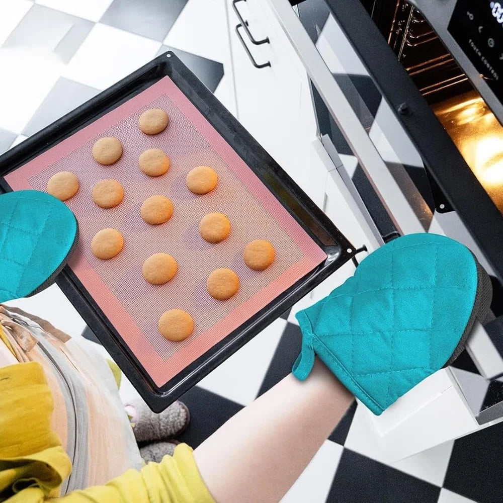 A hand is placing round silicone baking molds onto a baking sheet inside an oven, next to a pair of teal oven mitts.