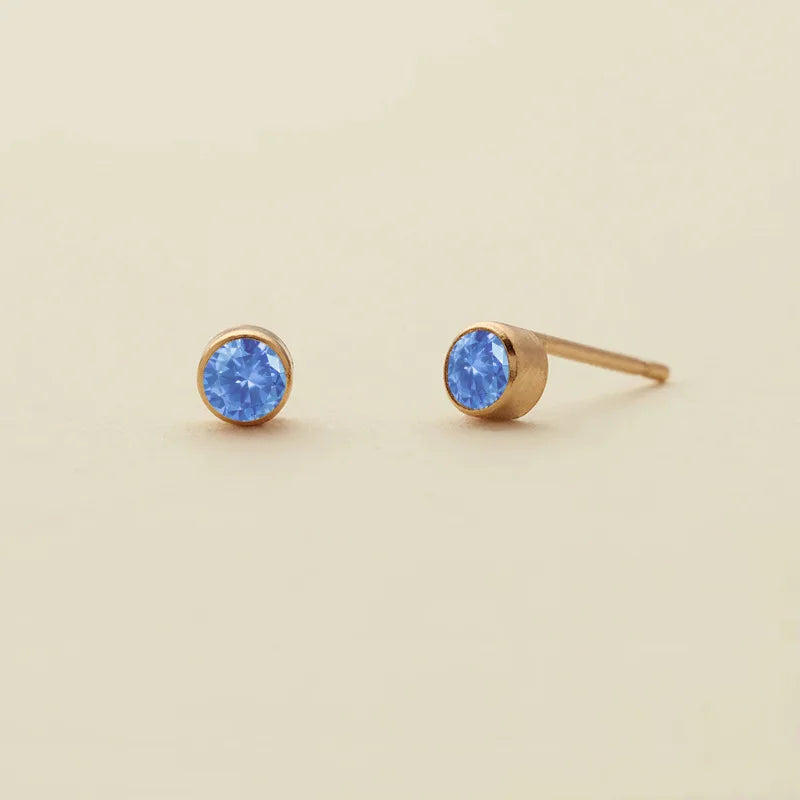 Boucles d'oreilles à clous de naissance en saphirs bleus ronds sur socles dorés.