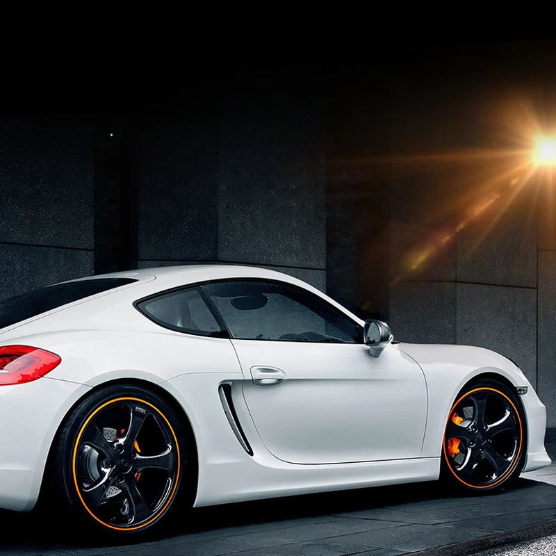 A white sports car is shown with orange rim protectors installed on the wheels against a dark background.