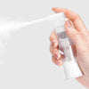 A hand is spraying a fine mist from a clear plastic bottle, likely a refillable spray for hair or travel.