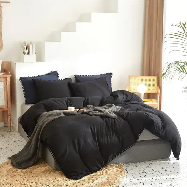 A black duvet cover set with pom tassels and gray bedding is displayed on a bed in a bright room.