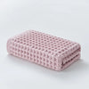 A stack of pink waffle weave bath towels folded neatly on a white surface.