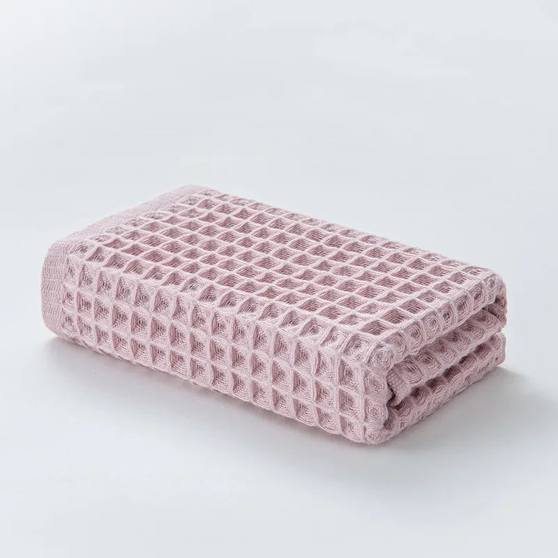 A stack of pink waffle weave bath towels folded neatly on a white surface.