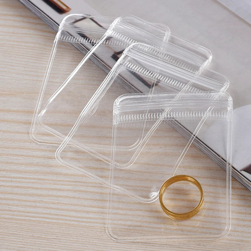 A stack of transparent PVC jewelry pouches with zip lock closures, featuring a gold ring.